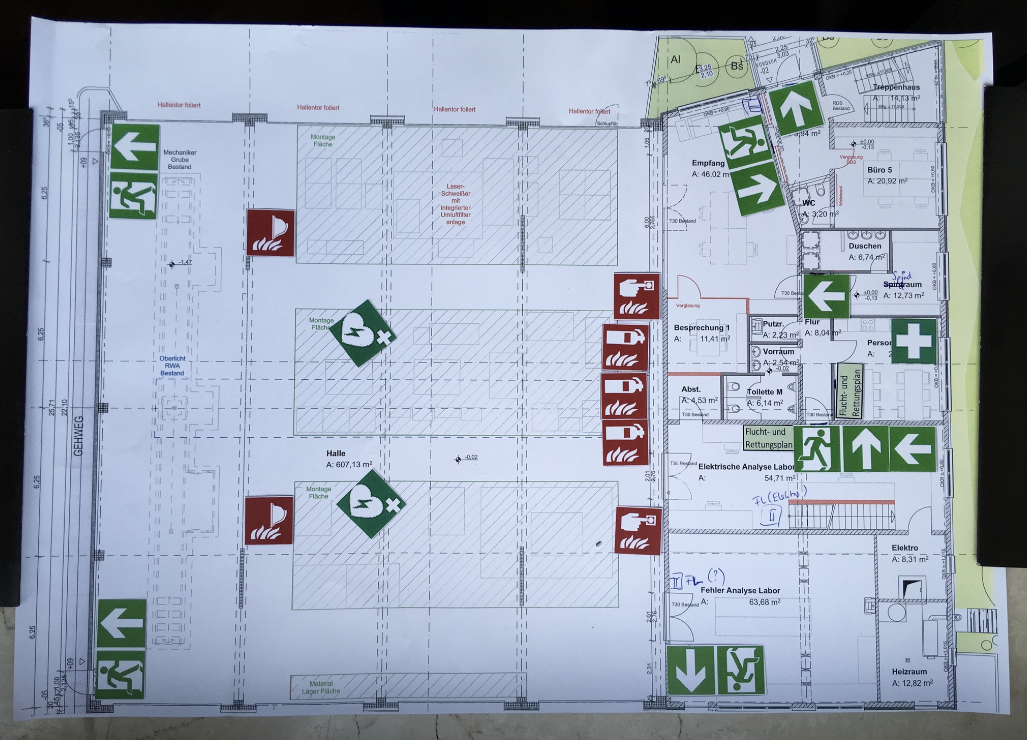 Das Foto zeigt den Übersichtsplan für den Prozess der Brandschutz Planung, bestehend aus einem geprinteten Gebäudegrundrissplan mit manuell aufgeklebten Elementen, z.B. Feuerlöscher, Notausgänge.