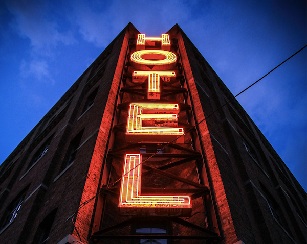 The photo shows a building façade photographed from below against the sky with the vertically mounted illuminated lettering &quot;HOTEL&quot;.
